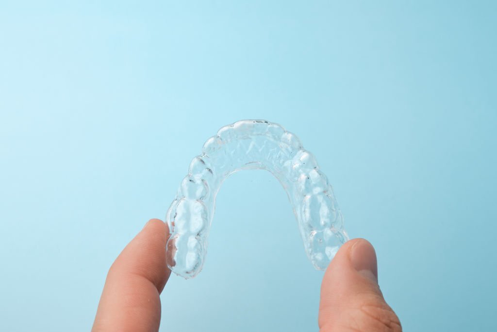 Close up mans hand holding a transparent removable braces for whitening teeth on a blue background with copy space. Invisible dental aligners for straighteners teeth