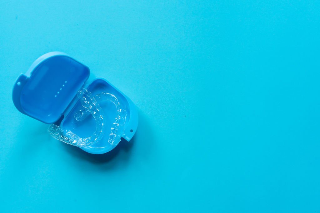 close up top view of dental aligner retainer (invisalign) on blue color background with copy space at dental clinic for beautiful teeth treatment course concept